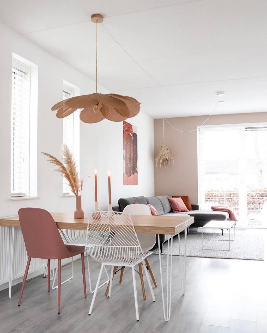 This Clérachic pendant lamp in tan petals hangs above a dining table set with striped candles and a pink wire chair.