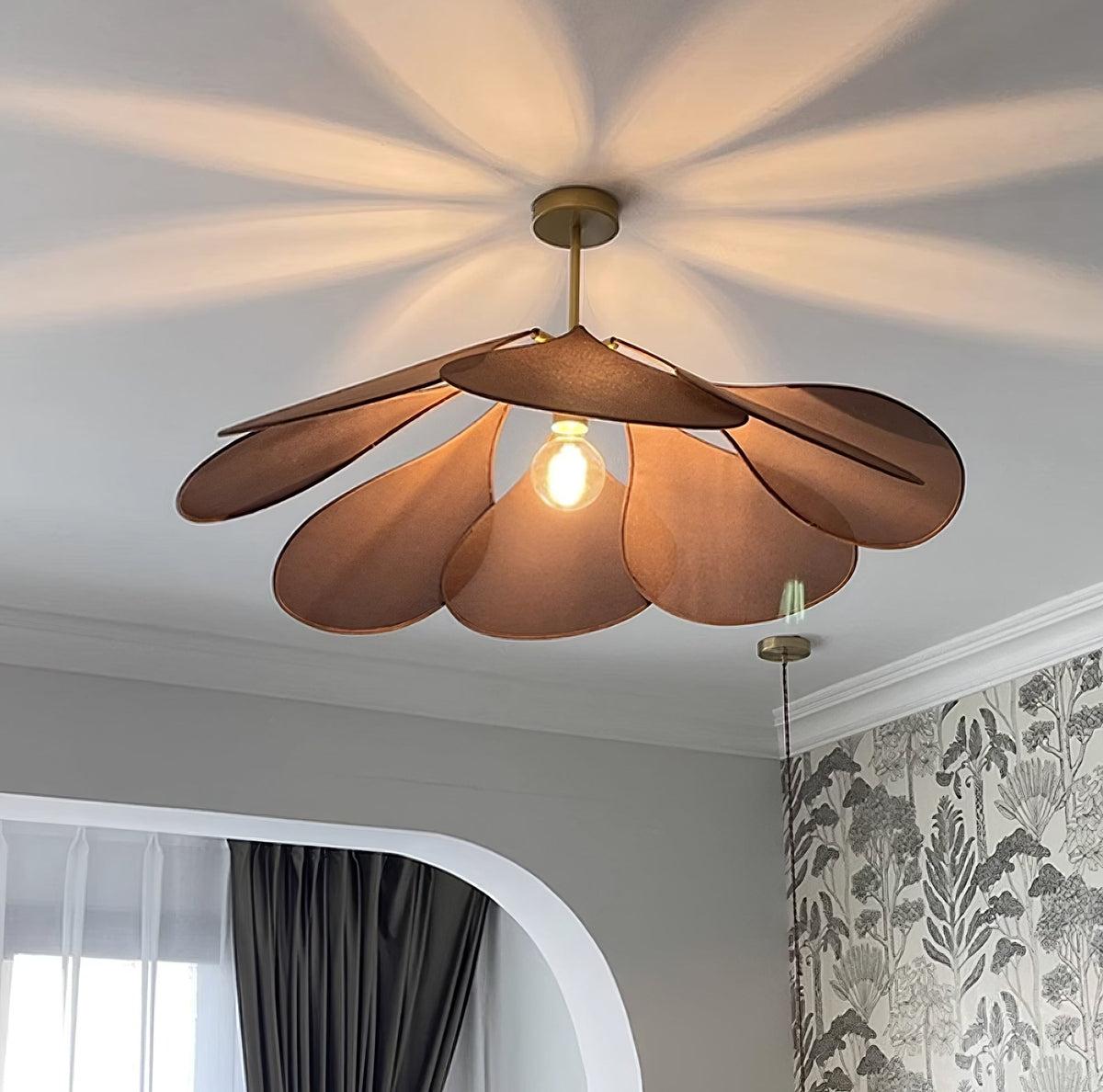 This Clérachic pendant lamp in deep rust petals glows warmly from below, casting a starburst shadow across the ceiling.