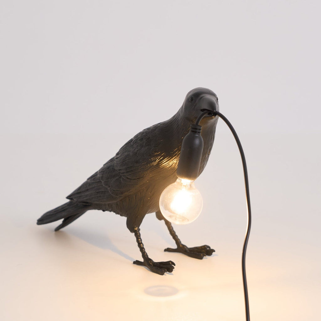 Raven table lamp lit warmly on a styled shelf