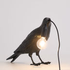 White raven lamp perched with an exposed filament bulb