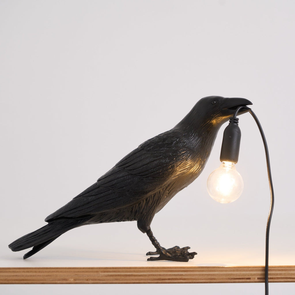 Black raven sculpture lamp glowing on a dark surface