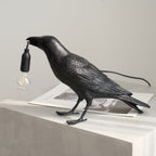 Black raven lamp perched with a warm filament bulb