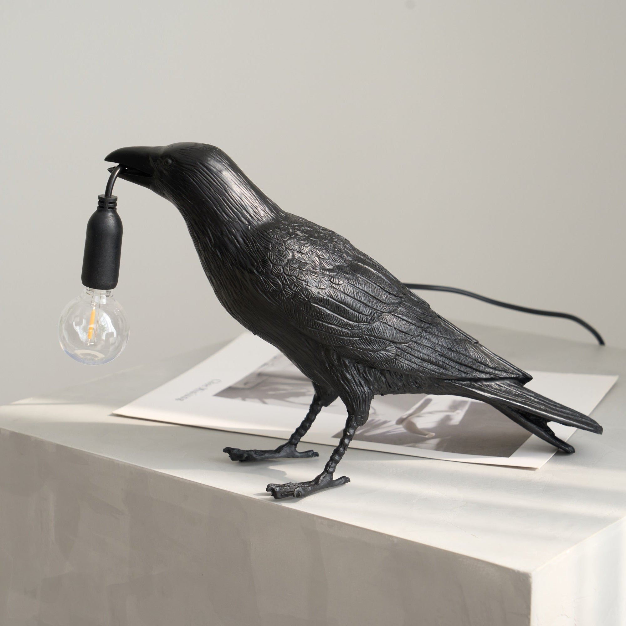 Black raven lamp perched with a warm filament bulb