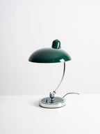 A green Clérachic desk lamp on a plain white backdrop, its cord trailing from the round base.