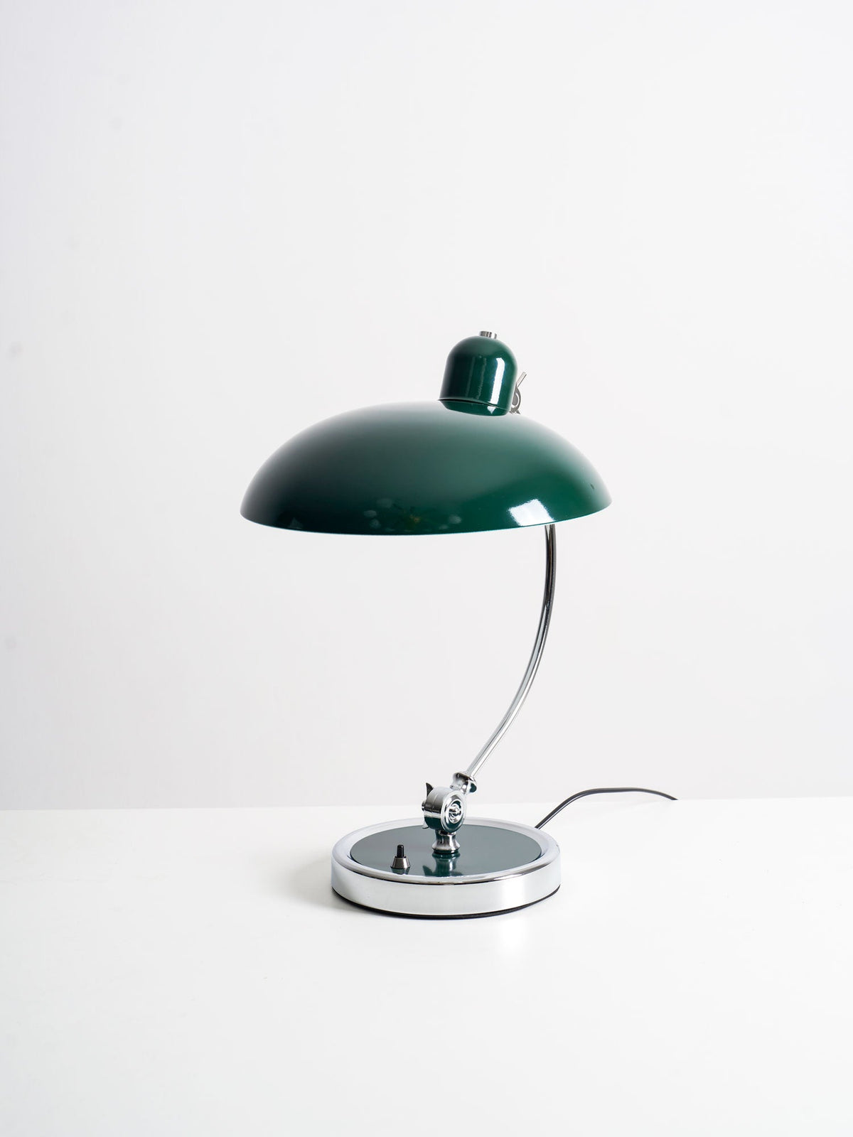 A green Clérachic desk lamp on a plain white backdrop, its cord trailing from the round base.