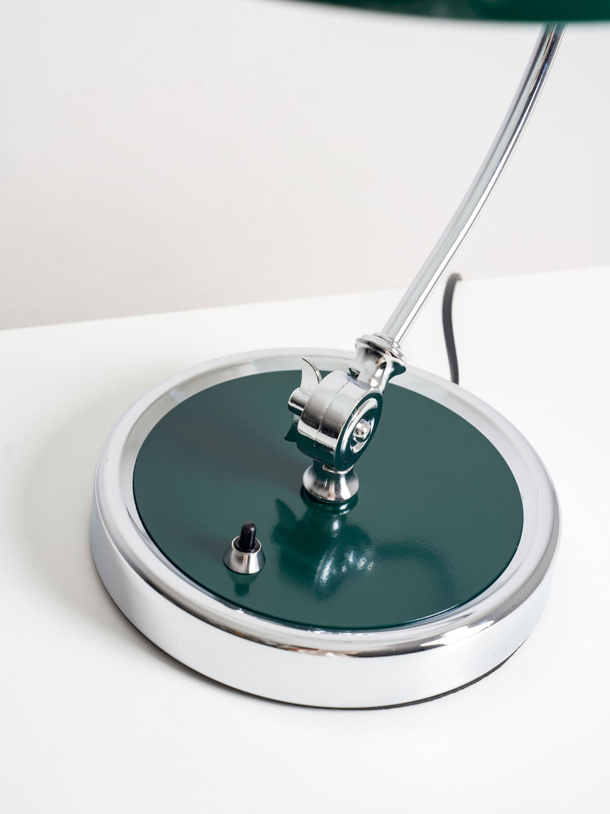 Close-up of the chrome joint and green base disc on this Clérachic desk lamp, with its cord visible.