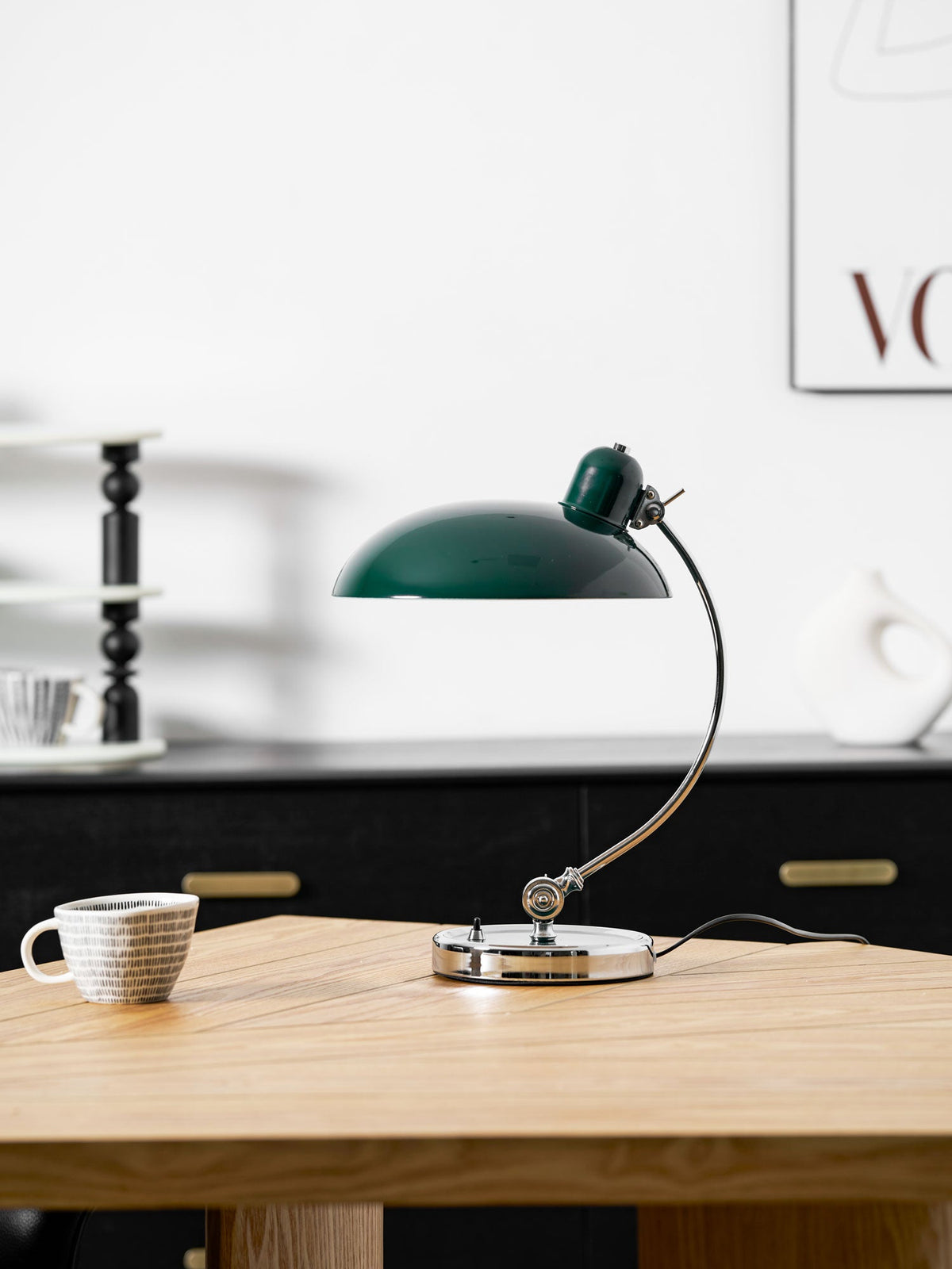 On a wood table beside a patterned cup, this green Clérachic desk lamp stands with black shelving soft behind it.
