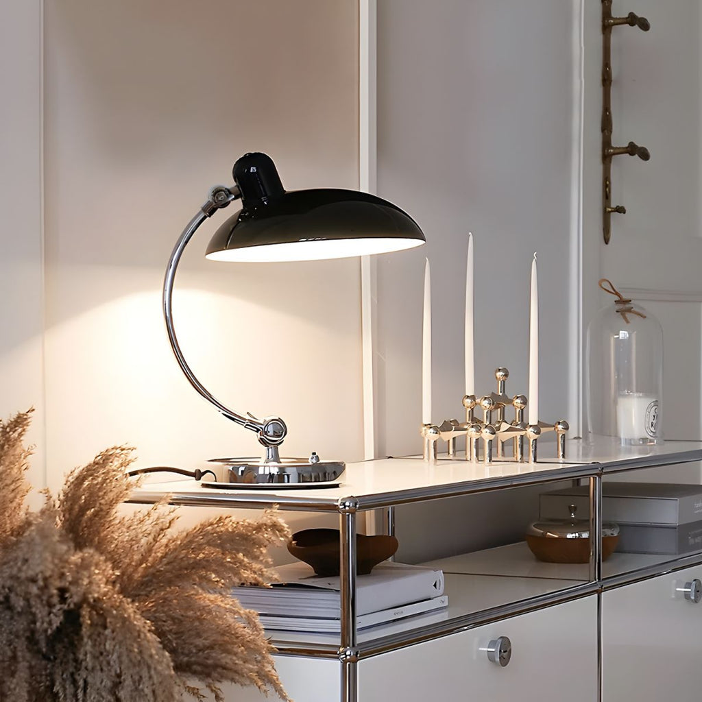 A black Clérachic desk lamp glows on a white sideboard beside pampas grass and candlesticks.