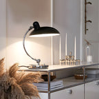 A black Clérachic desk lamp glows on a white sideboard beside pampas grass and candlesticks.