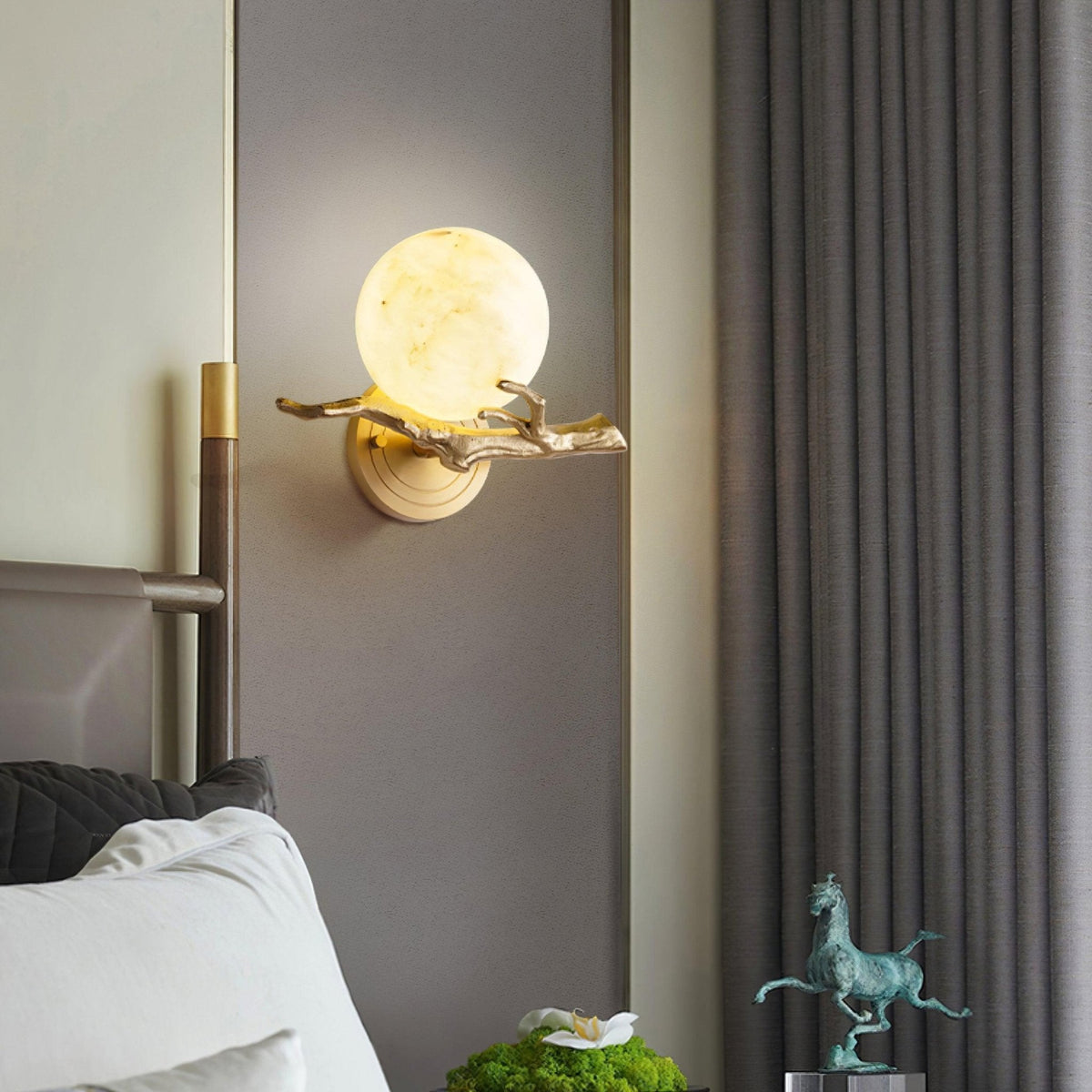 The lit Clérachic sconce is fixed beside a mirror reflecting a bronze horse figurine and a potted plant in a bedroom.