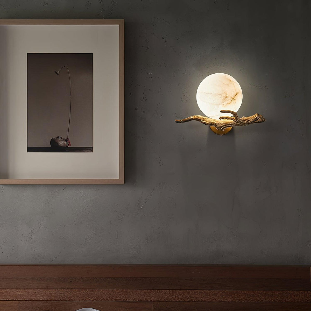 Mounted on a dark wall, the Clérachic sconce glows next to a framed still-life print above a dark wood console.