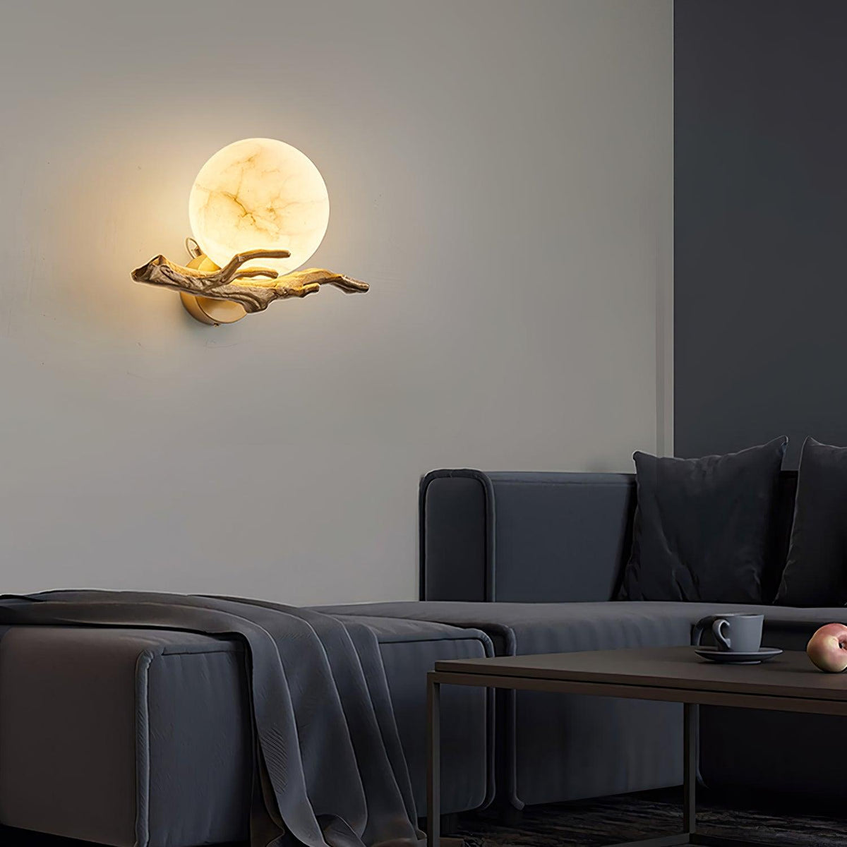 The Clérachic wall light glows softly above a dark grey sofa with a folded throw and a low wooden coffee table.