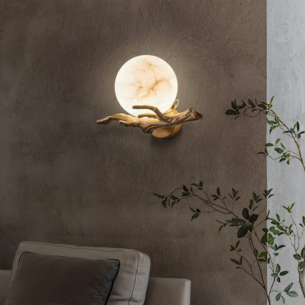 The lit Clérachic sconce sits on a two-tone dark wall above a sofa, with a trailing green plant to one side.