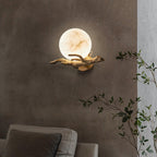 The lit Clérachic sconce sits on a two-tone dark wall above a sofa, with a trailing green plant to one side.