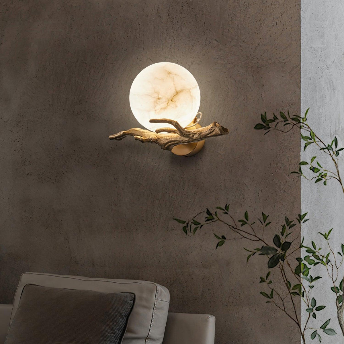 The lit Clérachic sconce sits on a two-tone dark wall above a sofa, with a trailing green plant to one side.
