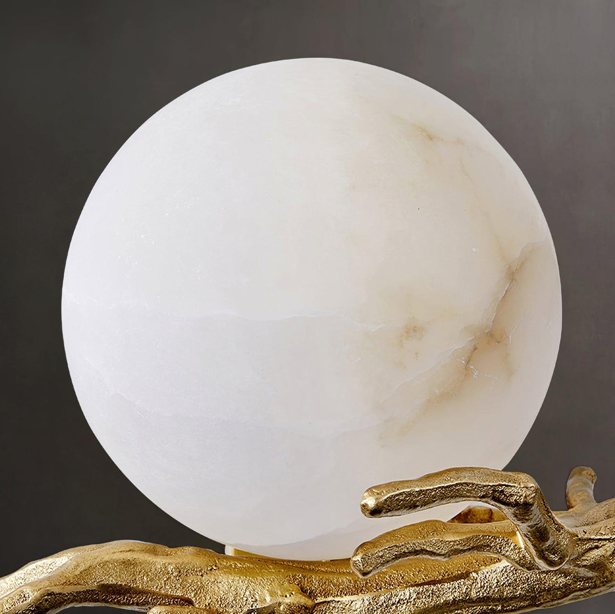A cooler-toned close-up of the marble shade on the Clérachic sconce, showing subtle grey veining above the brass arm.