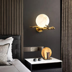 This Clérachic wall light glows above a dark leather headboard and a marble-topped nightstand holding cups and a tray.