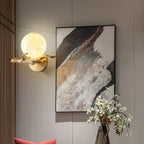 In a wood-panelled hallway, the Clérachic sconce glows beside framed abstract art and a vase of white flowers.