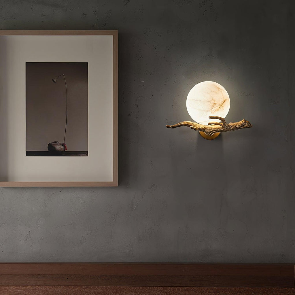 The lit Clérachic sconce hangs on a dark wall above a wood floor, beside a small framed still-life print.