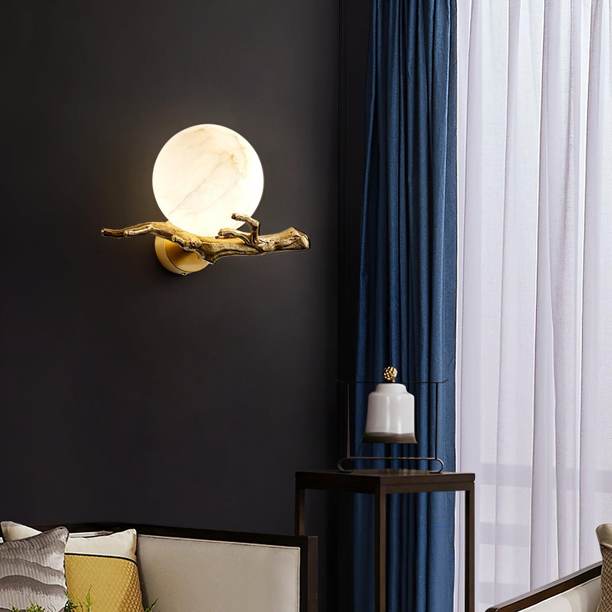 The lit Clérachic sconce sits beside a blue curtain and a small side table holding a white pillar candle.
