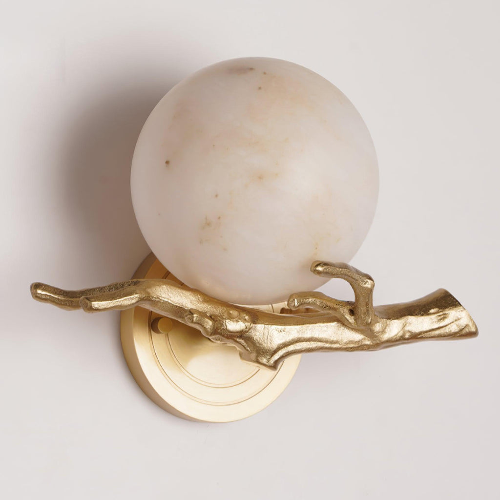 Close-up of the Clérachic sconce's round marble shade and cast-brass twig arm, unlit against a plain cream backdrop.