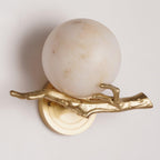 Close-up of the Clérachic sconce's round marble shade and cast-brass twig arm, unlit against a plain cream backdrop.