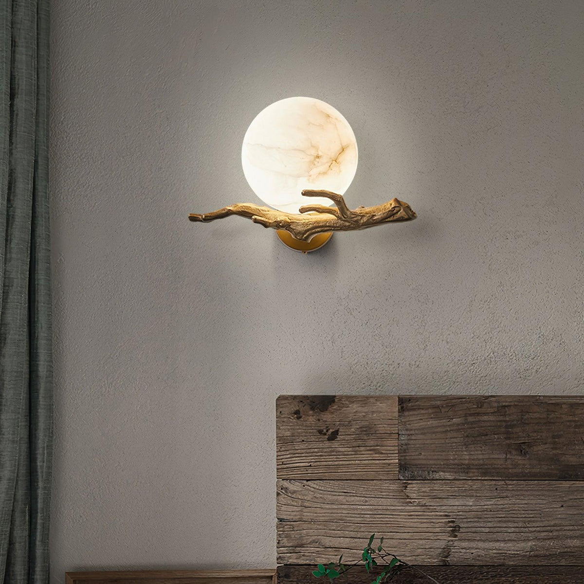 Mounted on a textured grey plaster wall, the Clérachic sconce glows beside a weathered plank of wood leaning nearby.