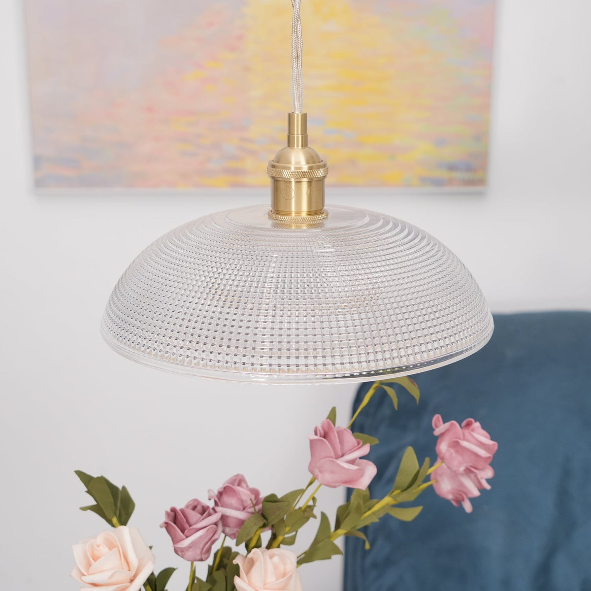 This Clérachic pendant hangs unlit near a blue sofa, pink roses in the foreground and a pastel painting behind.