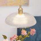 Close view of this Clérachic pendant's shade lit warmly above pink roses, blue sofa upholstery soft-focus behind.