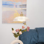 Unlit above a ring-shaped vase of pink roses, this Clérachic pendant hangs with a framed painting in the background.
