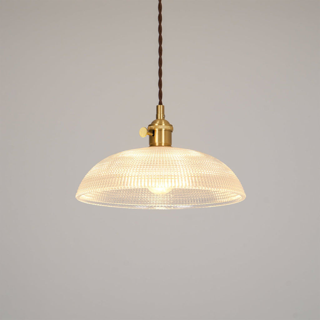 Lit against a plain off-white background, this Clérachic pendant's ribbed glass shade glows evenly around its brass fitting.