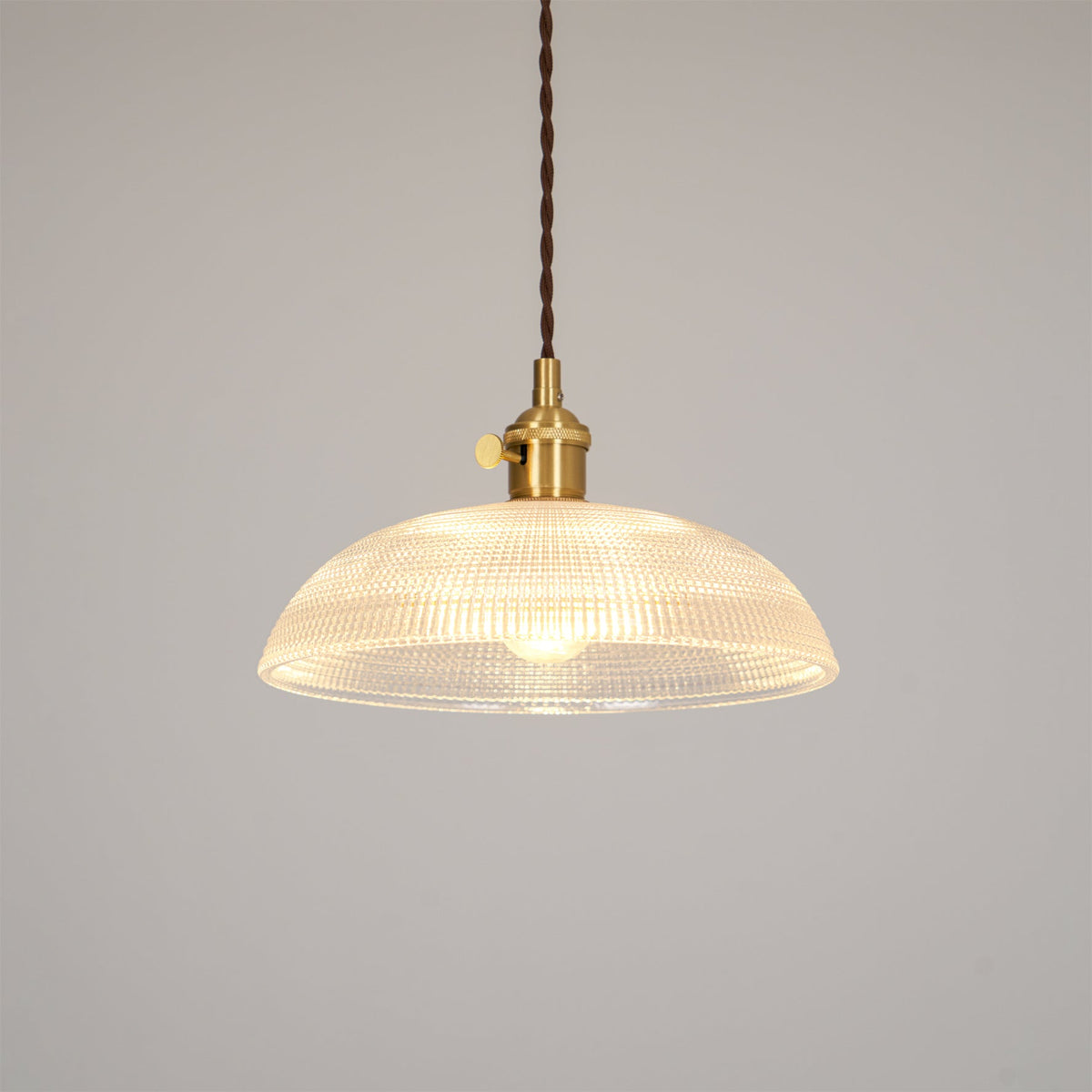 Lit against a plain off-white background, this Clérachic pendant's ribbed glass shade glows evenly around its brass fitting.
