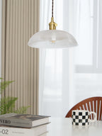 Hanging near a white curtain and a wood chair, this Clérachic pendant sits above books and a chequered mug.