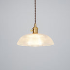 Lit against a plain grey background, this Clérachic pendant shows a dark twisted cord and brass fitting.
