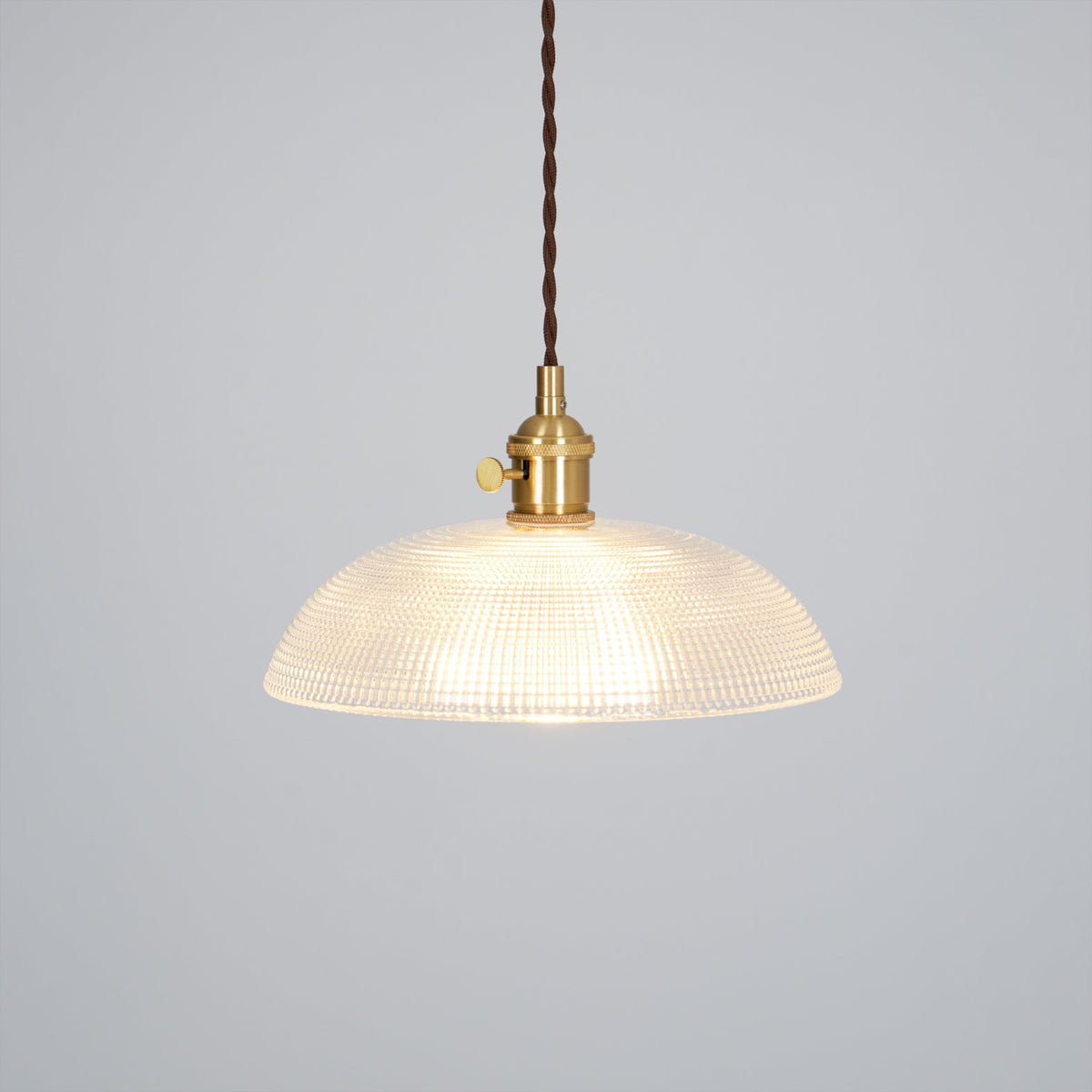 Lit against a plain grey background, this Clérachic pendant shows a dark twisted cord and brass fitting.