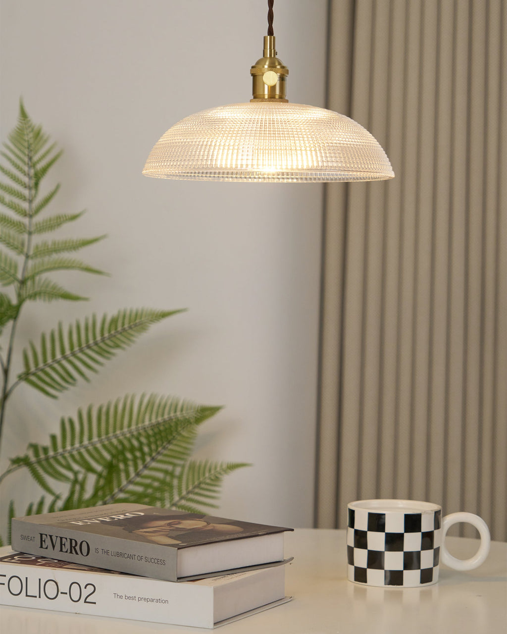 Near a curtained window with a fern in view, this Clérachic pendant hangs above books and a chequered mug.