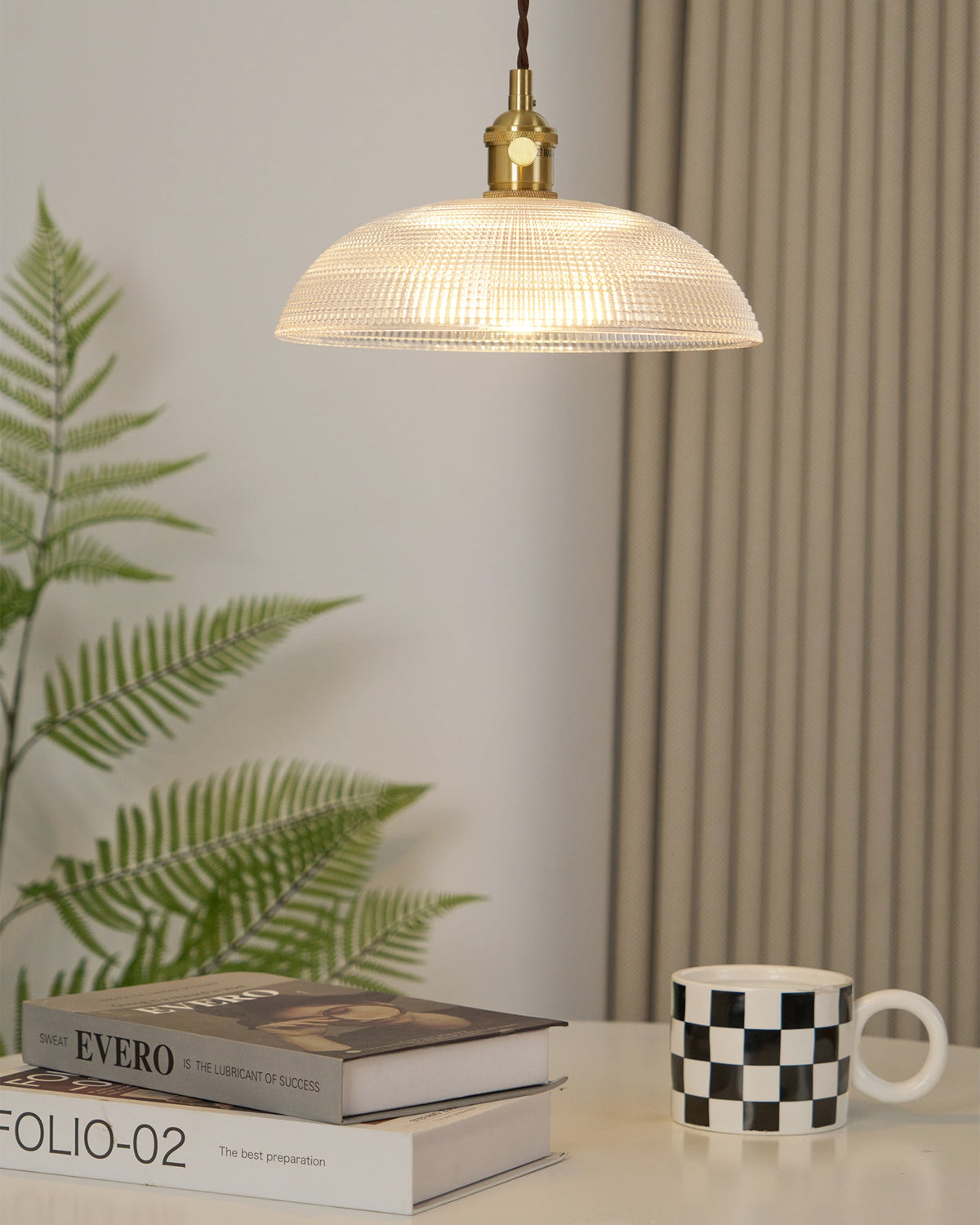 Near a curtained window with a fern in view, this Clérachic pendant hangs above books and a chequered mug.