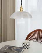 Hanging over a round table, this Clérachic pendant's ribbed glass shade sits above an open book and a chequered mug.