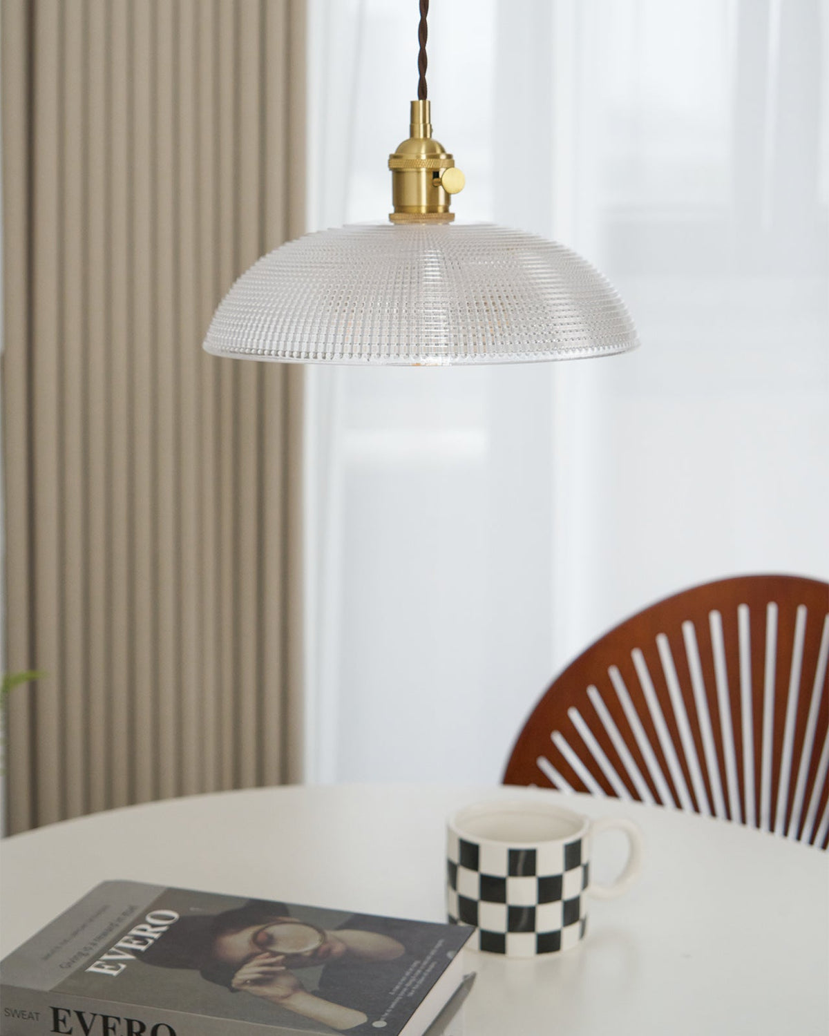 Hanging over a round table, this Clérachic pendant's ribbed glass shade sits above an open book and a chequered mug.