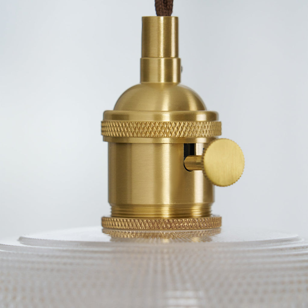 Extreme close-up of the brass socket hardware on this Clérachic pendant, its ribbed glass just visible below.