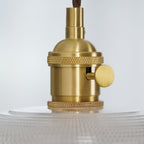 Extreme close-up of the brass socket hardware on this Clérachic pendant, its ribbed glass just visible below.