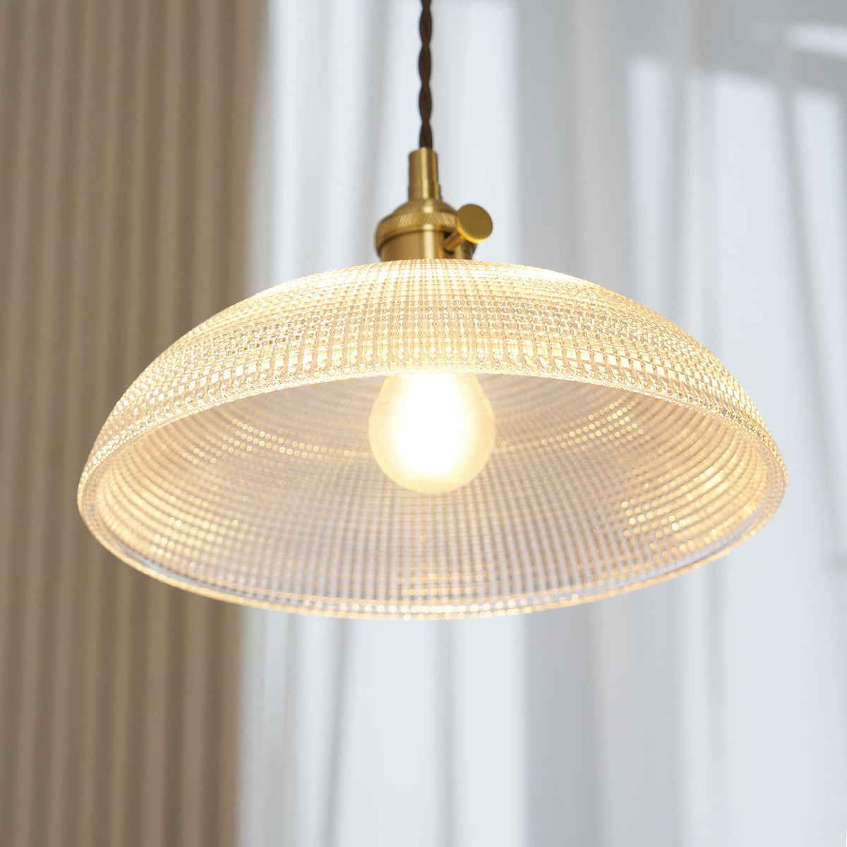 Seen from a low angle, the lit bulb glows beneath the ribbed glass dome of this Clérachic pendant.