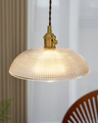 Near a curtained window, this Clérachic pendant hangs lit above a wood chair and a leafy plant.