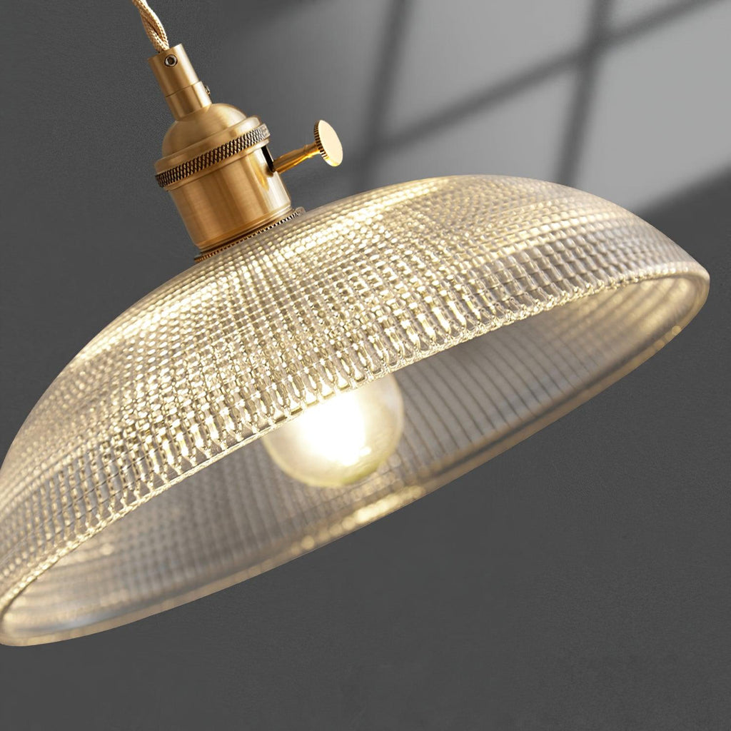 Close view from below this Clérachic pendant's lit shade, showing the bulb and ribbed glass as sunlight streaks the wall.