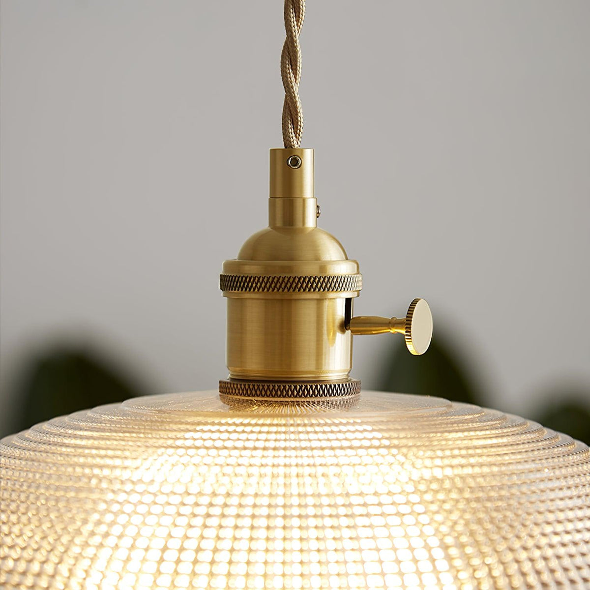 Close view of the brass socket and fitting atop the lit ribbed glass shade of this Clérachic pendant.