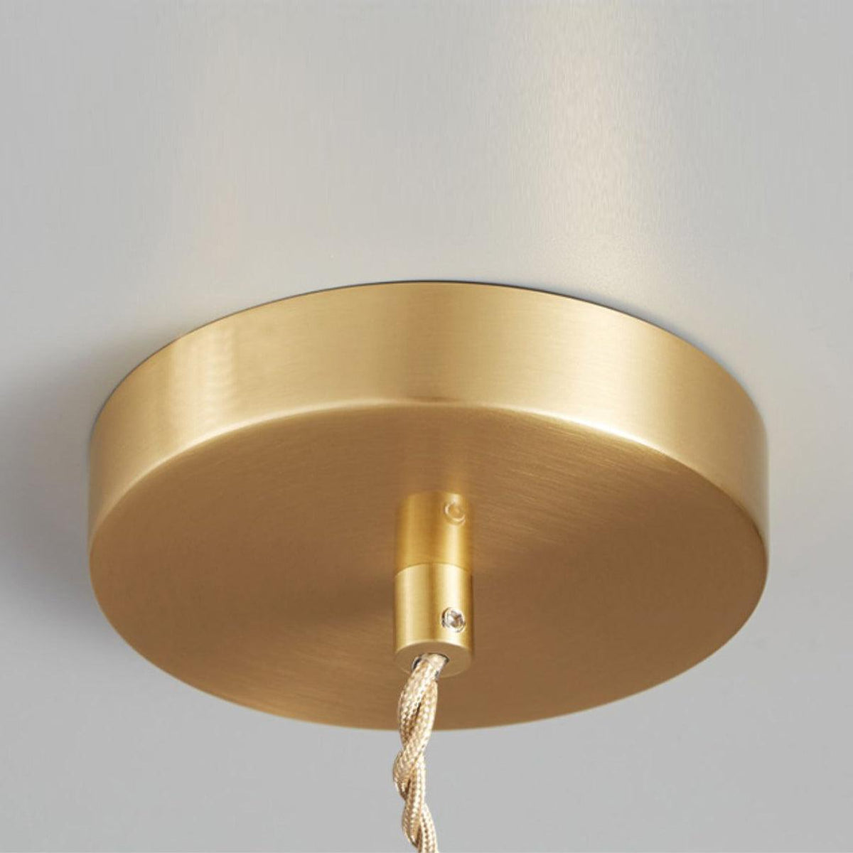 Close-up of the round brass ceiling canopy and cord for this Clérachic pendant, mounted on a white wall.
