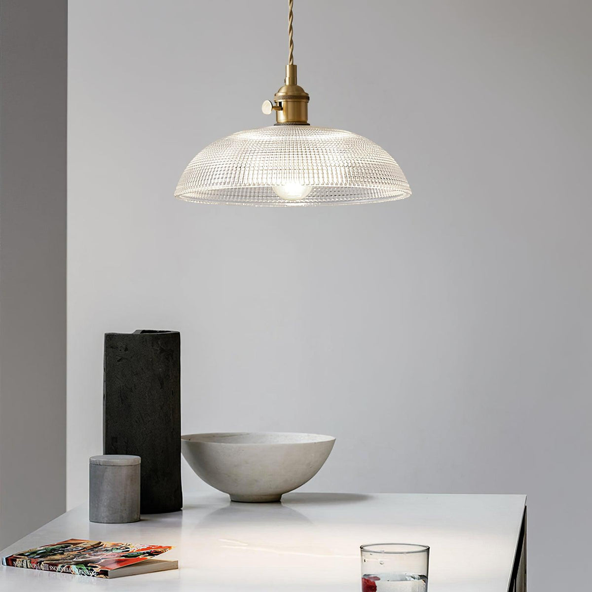 Lit above a white table set with a black vase and a pale stone bowl, this Clérachic pendant glows softly.