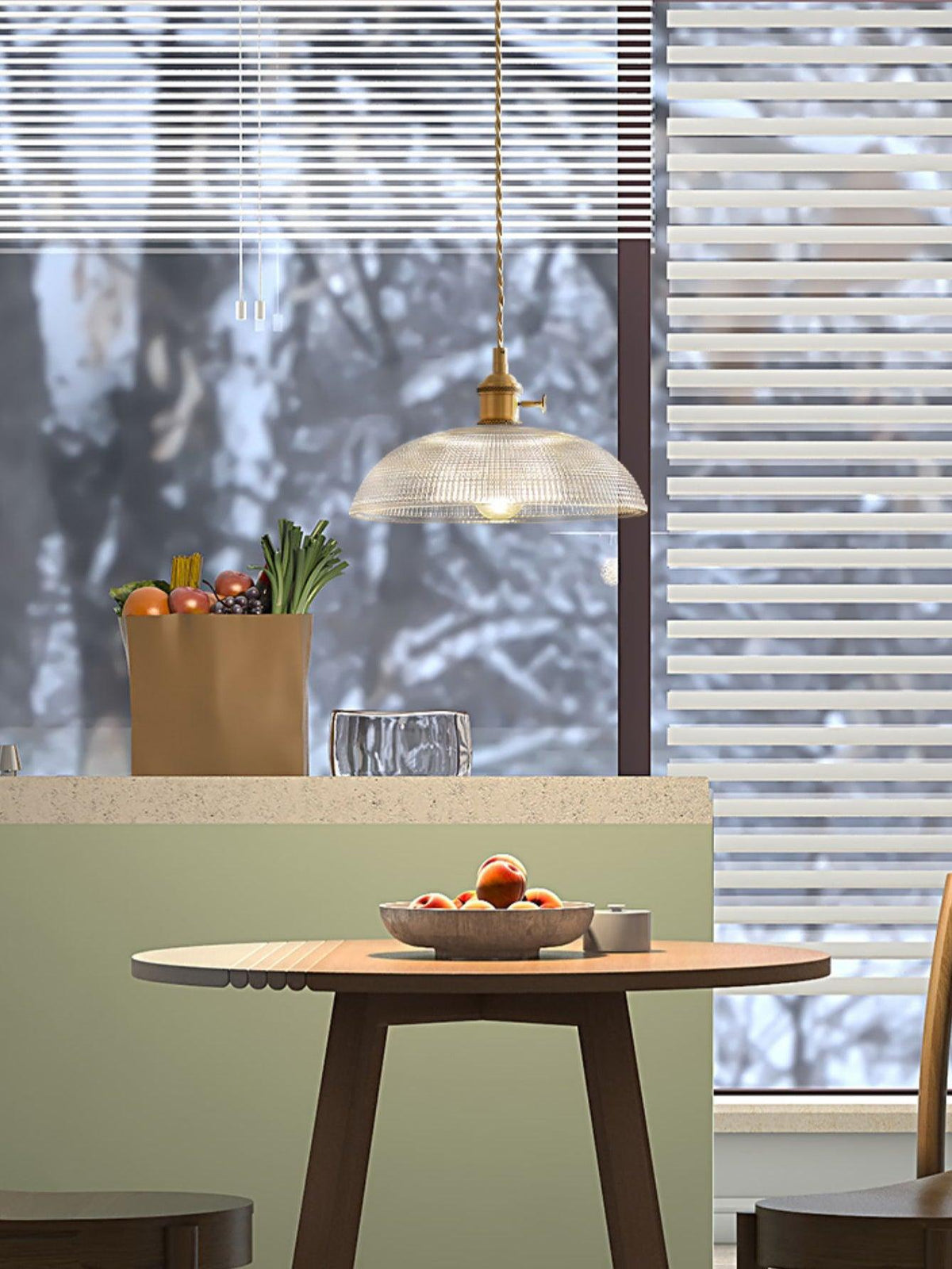 Near a window with striped blinds, this Clérachic pendant hangs above a counter set with a paper bag and a fruit bowl.
