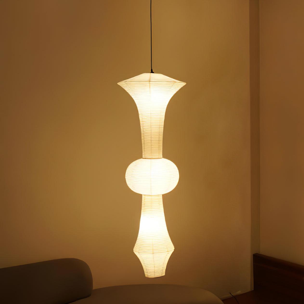 Tall mulberry paper pendant lit warm in an interior