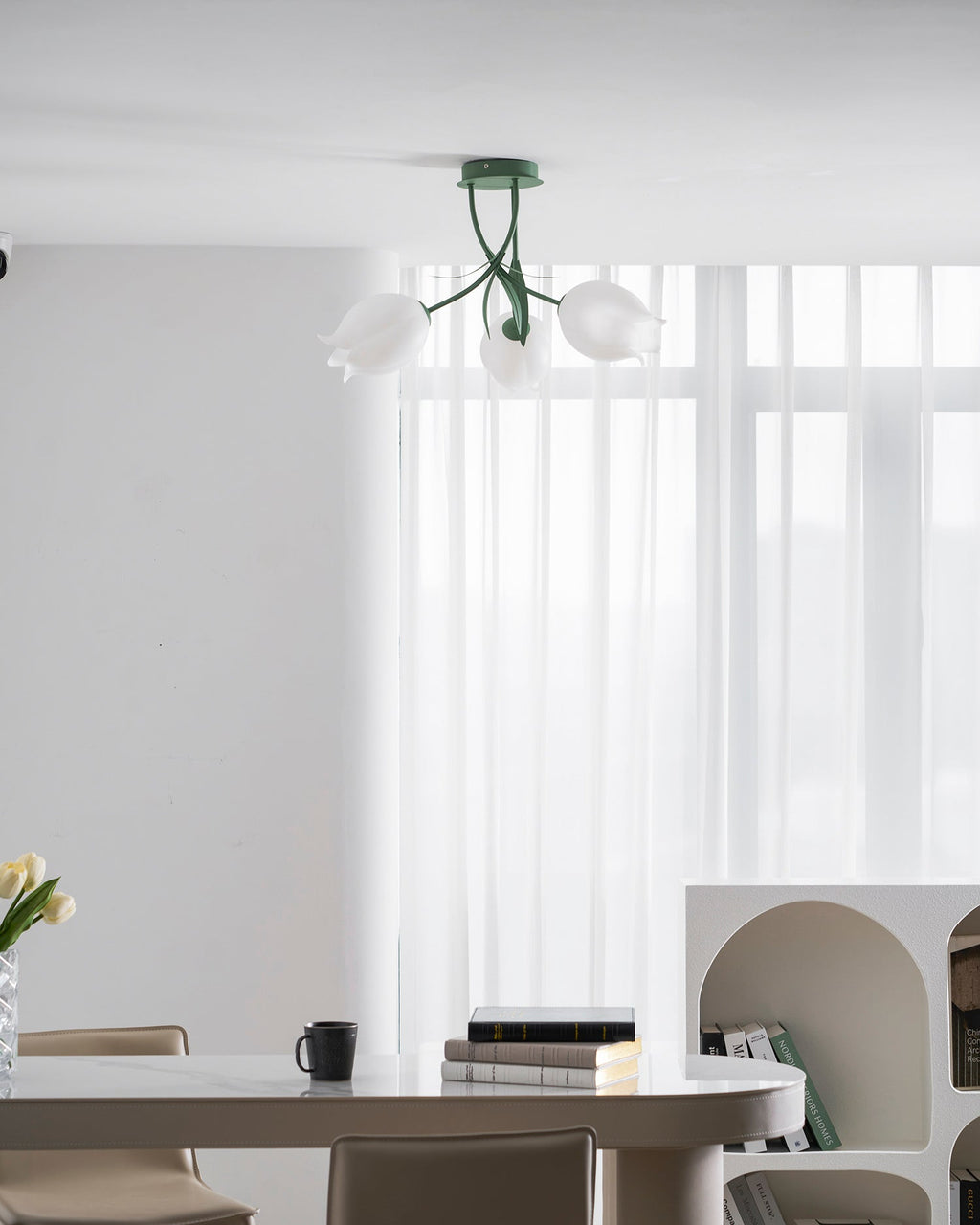 Above a dining table set with tulips, a mug and books, this Clérachic ceiling light in green hangs unlit.